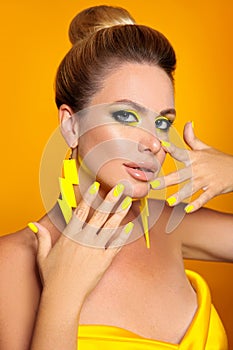 Beautiful girl with bright makeup isolated yellow background. Closeup portrait of blonde with manicured nails and glamour earrings