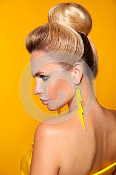 Beautiful girl with bright makeup isolated yellow background. Closeup portrait of blonde with manicured nails and glamour earrings