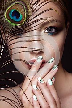 Beautiful girl with bright makeup, manicure design and peacock feather on her face. Art nails.