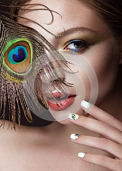 Beautiful girl with bright makeup, manicure design and peacock feather on her face. Art nails.