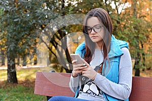 Beautiful girl in glasses sits on a bench and writes and reads S