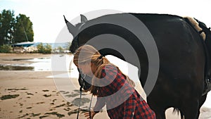 Beautiful girl cares for her horses on beach. Focus on the girl.