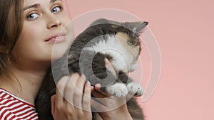 Beautiful girl with a cat in her arms on a pink studio background, profile of the face of a young woman caressing a pet, pet conce