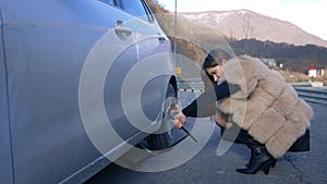 Beautiful girl changing the wheel of a car parked on the roadside