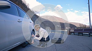 Beautiful girl changing the wheel of a car parked on the roadside