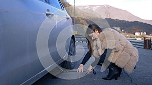 Beautiful girl changing the wheel of a car parked on the roadside