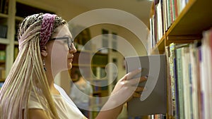 Beautiful girl chooses a book in the library