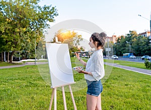 Beautiful girl city summer, woman artist, draws picture road, beginning of drawing, white canvas painting, easel stand