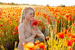 A beautiful girl with closed eyes meditates on a poppy field holding a bouquet of flowers