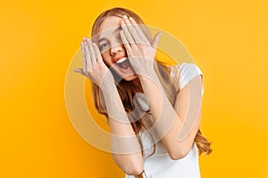 Beautiful girl closes her eyes with her hands, on a yellow background, playing hide and seek