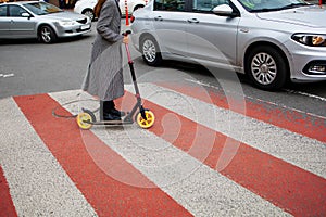 Beautiful Girl In A Coat Rides Electric Scooter on a pedestrian crossing In The City