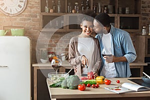 Beautiful girl cooking while her boyfriend kissing her in cheek