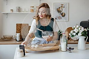 Beautiful girl cooks and looks at the recipe on the smartphone