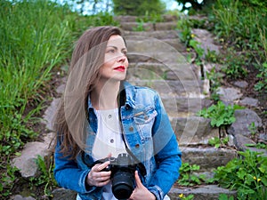 Beautiful girl in a cotton jacket sits on vintage stone steps and taking photos with a professional camera in windy weather