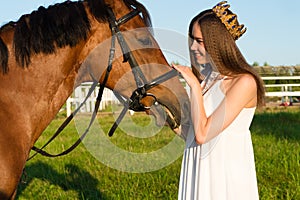 Beautiful girl with a crown caress horse