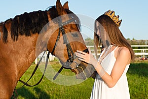 Beautiful girl with a crown caress horse outdoors