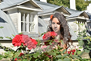 Beautiful girl with curls next to red roses in the garden