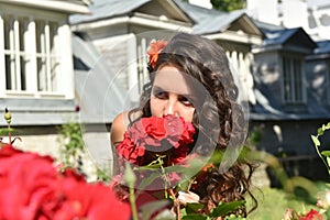 Beautiful girl with curls next to red roses in the garden