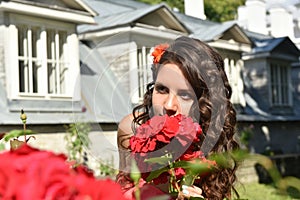 Beautiful girl with curls next to red roses in the garden