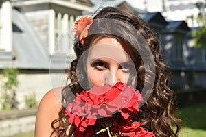 Beautiful girl with curls next to red roses in the garden