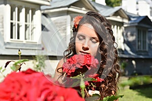 Beautiful girl with curls next to red roses in the garden