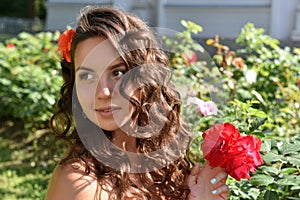 Beautiful girl with curls next to red roses in the garden