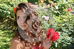 Beautiful girl with curls next to red roses in the garden