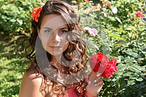 Beautiful girl with curls next to red roses in the garden