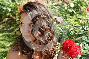 Beautiful girl with curls next to red roses in the garden