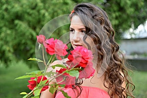 Beautiful girl with curls next to red roses in the garden