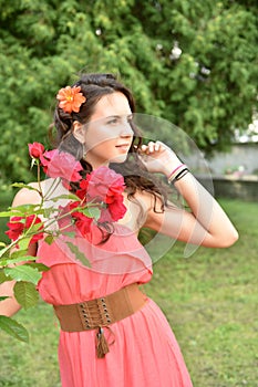 Beautiful girl with curls next to red roses in the garden