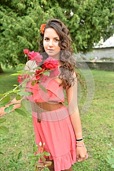 Beautiful girl with curls next to red roses in the garden
