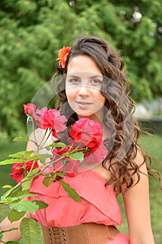 Beautiful girl with curls next to red roses in the garden