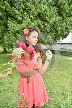 Beautiful girl with curls next to red roses in the garden