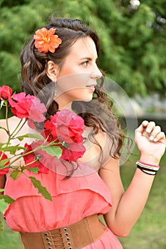 Beautiful girl with curls next to red roses in the garden