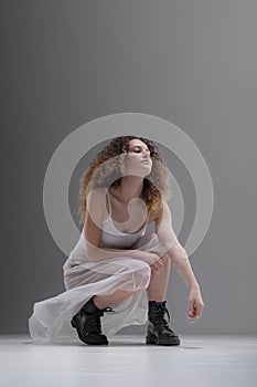 Beautiful girl with curly hair. Ballerina in white dress and black boots