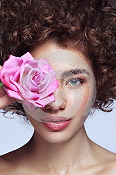 Beautiful girl with curly hair, clean makeup and pink rose in her hand