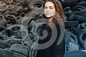 Beautiful girl, curly hair, portrait on the background of dump old car tires. Looking left