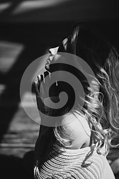 A beautiful girl with curly hair sits on the floor in the sunshine folded her hands in prayer to God. Black and white art photo.