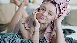 Beautiful girl cutely smiling in blue contact lenses and shiny earrings. Pretty smiley married girl lies on a big bed