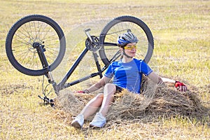 Beautiful girl cyclist sitting on dry grass on the background of the bike. Nature and man