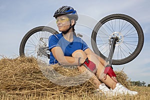 Beautiful girl cyclist sitting on dry grass on the background of the bike. Nature and man