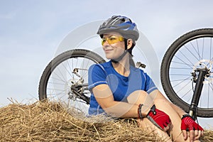 Beautiful girl cyclist sitting on dry grass on the background of the bike. Nature and man