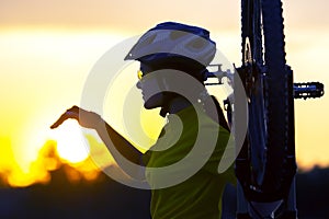 Beautiful girl cyclist touches the setting sun with her hand. Sports and recreation. Nature and man