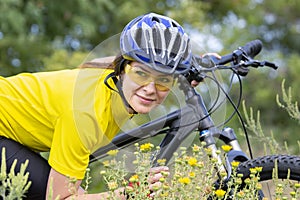 Beautiful girl cyclist in the yellow field sniffing flowers. Sports and recreation. Nature and man