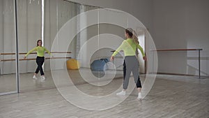 A beautiful girl dances in front of a mirror and preens during a dance workout in the gym