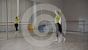A beautiful girl dances in front of a mirror and preens during a dance workout in the gym
