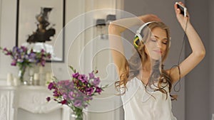 Beautiful girl is dancing in headphones in her luxurious apartment