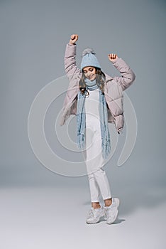 beautiful girl dancing in warm coat, knitted hat and scarf on grey.