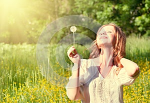 Beautiful girl with dandelion enjoying summer sun